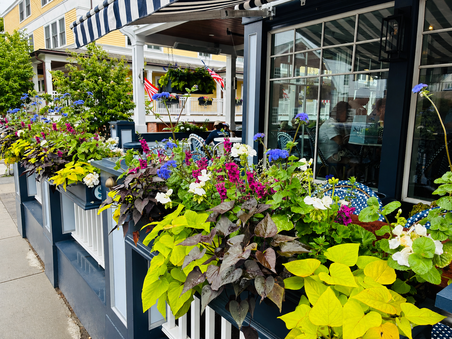A sunny outdoor restaurant patio with flowers, striped awnings, and waterfront charm