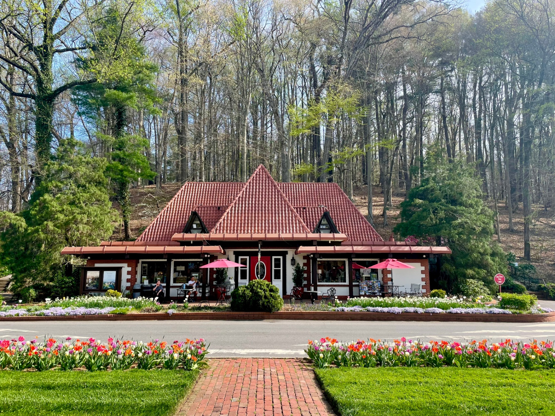 A charming cottage-style building with a red roof surrounded by spring tulips and trees